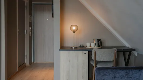 Et hyggeligt hotelværelse med et skrivebordsområde, en varm lampe og en elkedel til varme drikke, ved siden af et behageligt siddeområde.