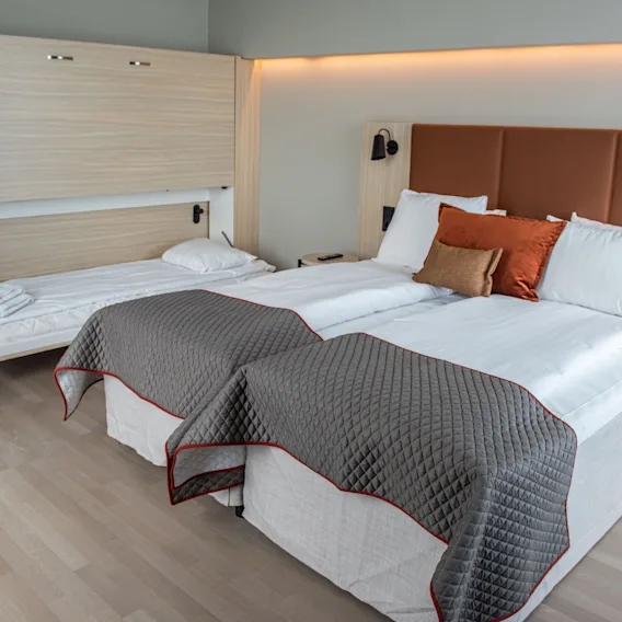 Ett modernt hotellrum med två bekväma sängar och en extra nedfällbar säng, vilket erbjuder flexibla sovplatser.