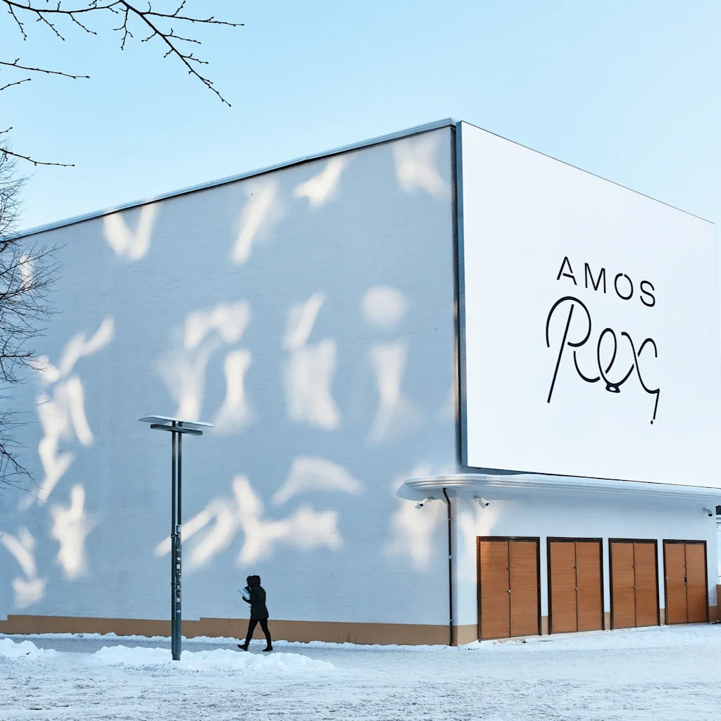 Amos Rex art museum on a bright winter day. A person walks past the white building, where sunlight casts playful shadows.