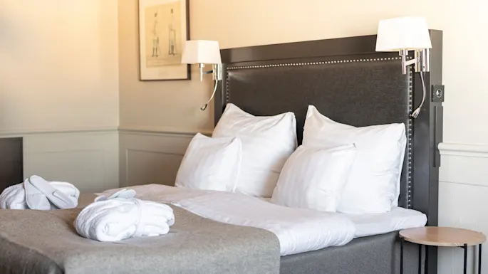 A comfortable hotel room with a neatly made bed, white bathrobes, and slippers, suggesting a relaxing stay.