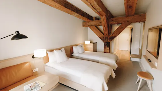Ett mysigt hotellrum med två enkelsängar, synliga takbjälkar i trä och en bekväm sittgrupp.