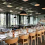 Et moderne restaurantområde med lange bord dekket for gjester, med store vinduer som vender ut mot en naturskjønn utsikt.