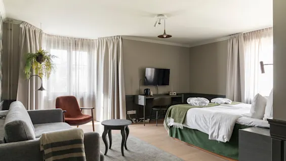 Kutsuva hotellihuone, jossa on mukava sänky, viihtyisä oleskelualue ja toimiva työpiste valoisan ikkunan äärellä.