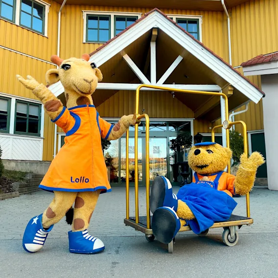 Maskottene Lollo giraff og bjørnen Bernie på en bagasjevogn utenfor hotellinngangen.