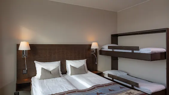 Ljust hotellrum med en dubbelsäng och en mysig våningssäng i trä.