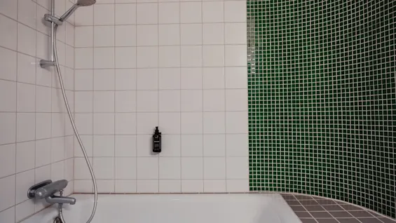 A modern bathroom at Home Hotel Uppsala with a bathtub and shower, featuring white and green mosaic tiled walls.