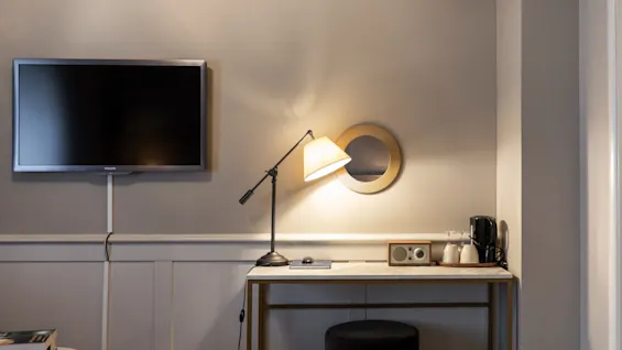 En bekväm hotellrumsinredning med en väggmonterad TV, ett väl upplyst skrivbord med en radio och en kaffebryggare.