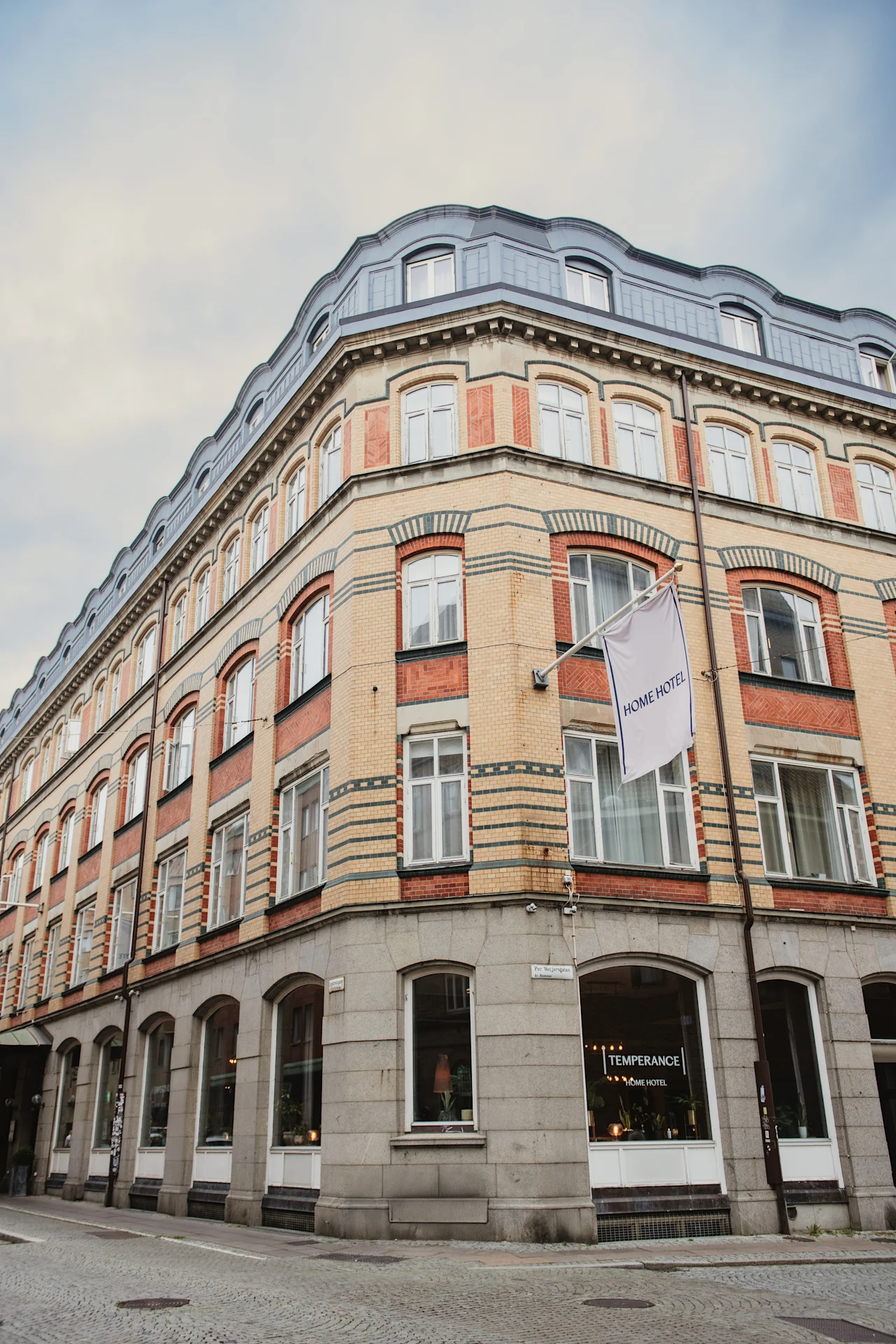 En fleretagers bygning med buet tag og murstensfacade. Et flag viser HOME HOTEL, og et vinduesskilt lyder TEMPERANCE HOME HOTEL.