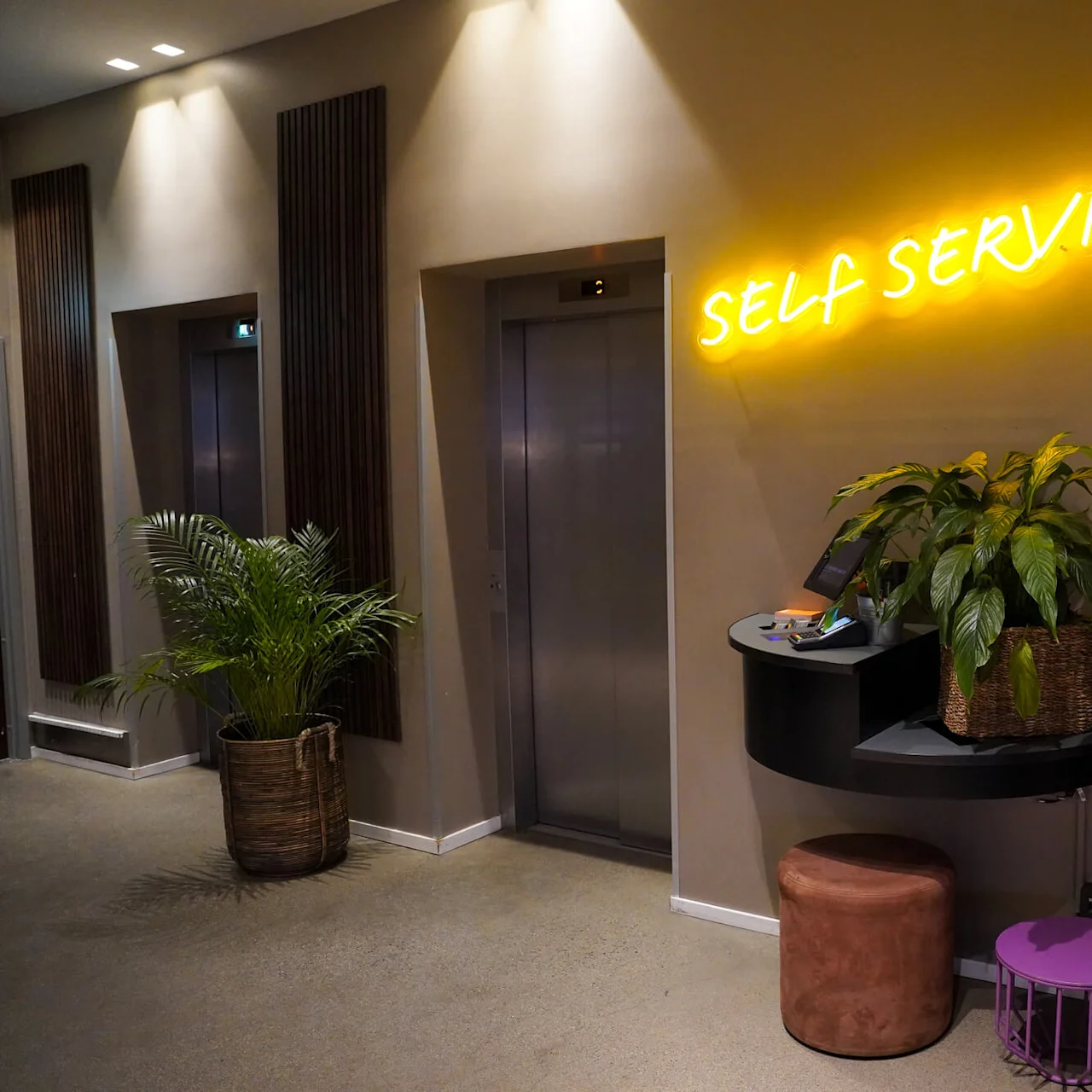Neonskiltet siger "SELF SERVICE" over en service station med planter, to elevatorer i nærheden.