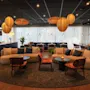 En sittgrupp med moderna soffor och stolar är arrangerad runt små bord. Omgivande hängande lampor ger en mysig atmosfär i en stilfullt inredd lounge.