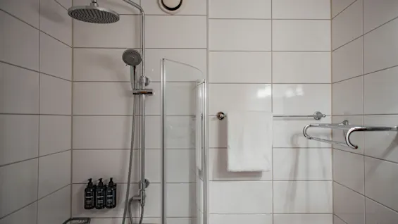 Ett rent, modernt duschutrymme med vita kakelplattor, en regndusch och toalettartiklar. En fräsch handduk hänger i närheten.