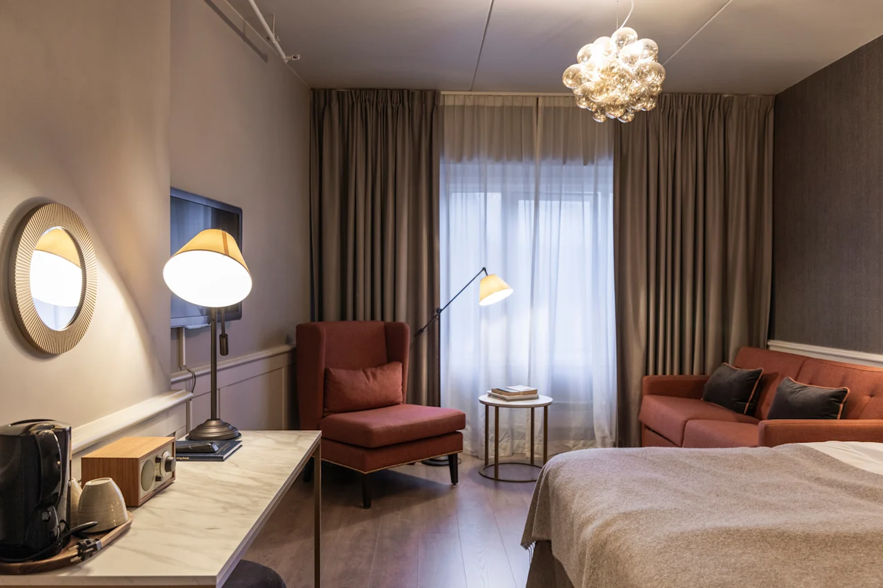 A warm and inviting hotel room at Home Hotel Grand Bodø, featuring comfortable seating, a workspace, and soft lighting.