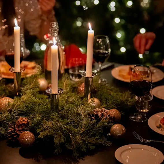 En festlig dukning med tända ljus, vinglas och en julgirlang som mittpunkt.