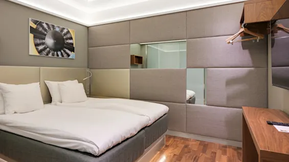 Ett modernt hotellrum med en snyggt bäddad dubbelsäng med vita sängkläder. Väggkonst, eleganta trämöbler och mjuk belysning skapar en minimalisk, mysig atmosfär.