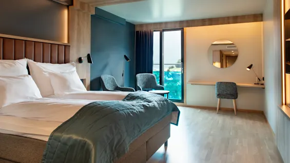 Et moderne hotelværelse med en stor seng, et skrivebord og en balkon med naturskøn udsigt.