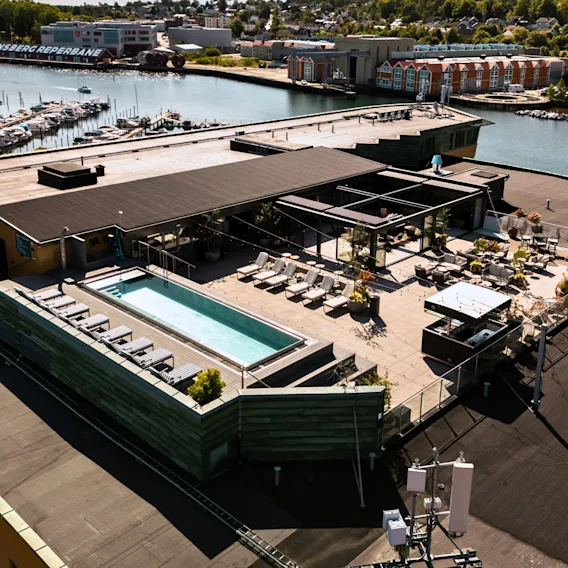 Luftfoto av en takterrasse på et hotell med svømmebasseng, solsenger, utendørs lounge og utsikt over havnen.
