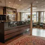Tyylikäs hotellibaari ja lounge-alue, jossa on tumma puinen baari, mukavat istuimet, suuret ikkunat ja punainen kuvioitu matto. Poistumisnuoli.