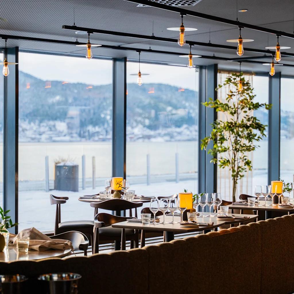 En elegant spisestue med dækkede borde og et fantastisk vinterlandskab synligt gennem store vinduer.