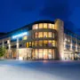 En stor hotellbygning med skiltet "Quality Hotel Sogndal" er opplyst om natten. Den står med moderne arkitektur i et åpent, brosteinsbelagt gårdsplass under en klar, dypblå himmel.