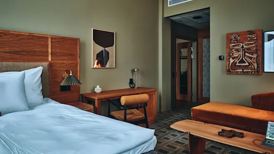 Et koselig hotellrom med en komfortabel seng, et skrivebord for arbeid og et stilig sitteområde for avslapning. Kunst pryder veggene.