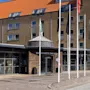Hotellets indgang med skiltet "QUALITY HOTEL THE REEF" er omgivet af høje flagstænger. Bygningen har flere vinduer, et orange tegltag og en klar blå himmel i baggrunden.