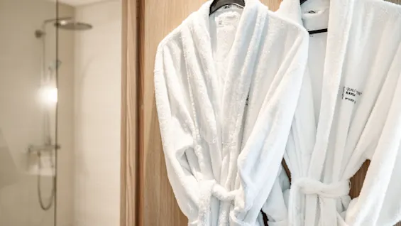 Two white bathrobes hanging on wooden hooks, next to a modern shower area. Text on robes: “I am qualified to be a star for whatever I want.”