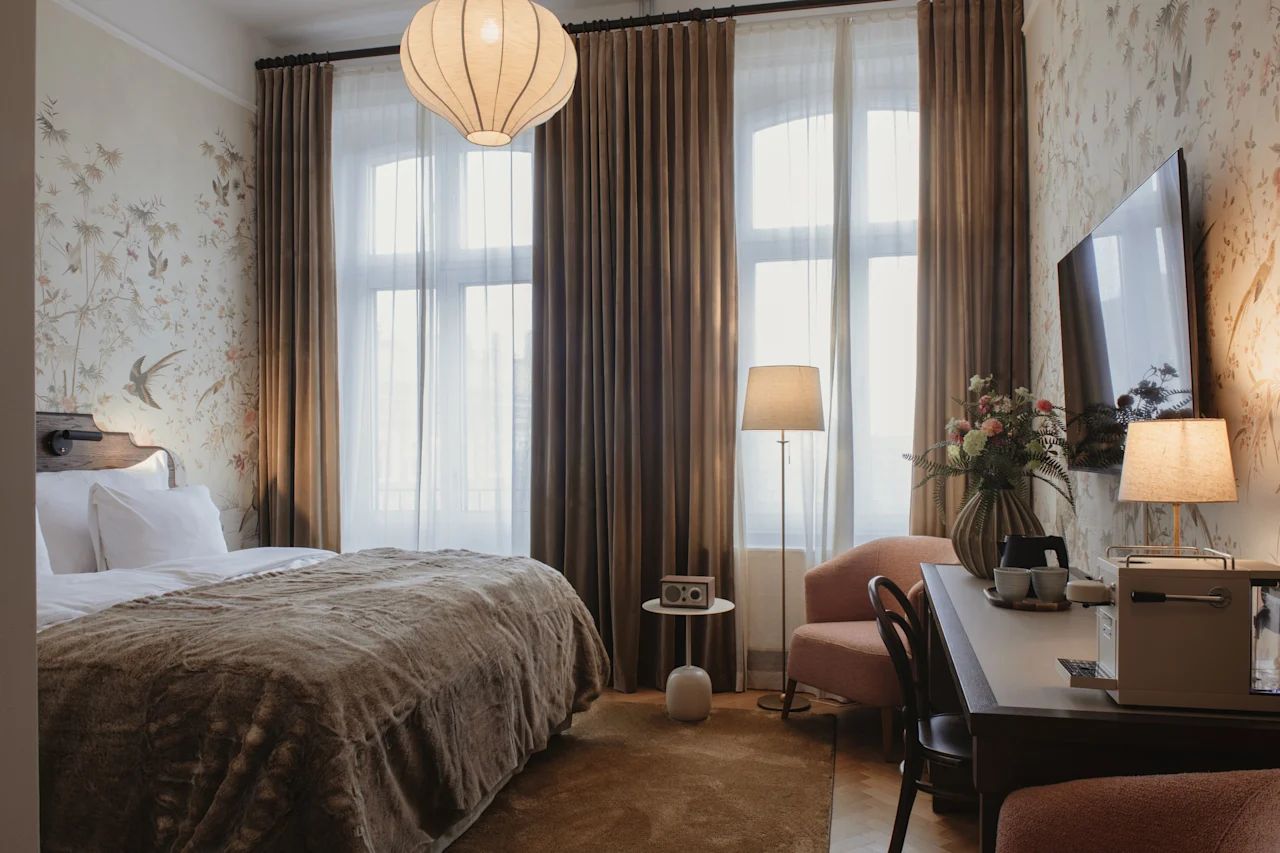 Home Hotel Baltzar - Deluxe Double. A cozy hotel room with a comfortable bed, a desk area, and large windows with curtains.