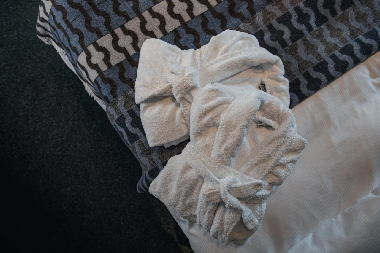 Two soft white bathrobes neatly folded on a bed, inviting comfort and relaxation.