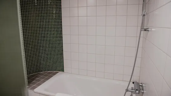 Siisti kylpyhuone Home Hotel Uppsalassa, jossa on valkoinen kylpyamme, suihku ja kaakeloidut seinät.