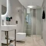 A modern bathroom with a white toilet, sink, mirror with backlight, and a transparent shower stall, with beige tiles.