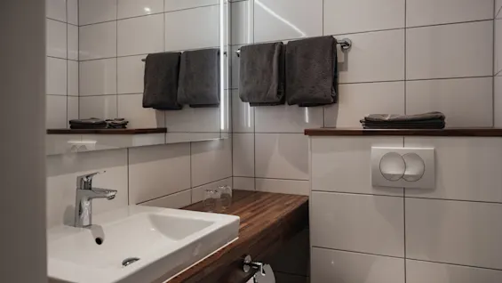 Siisti ja moderni kylpyhuone Home Hotel Victoriassa, jossa on valkoinen pesuallas, puinen taso, valaistu peili ja puhtaat pyyhkeet.