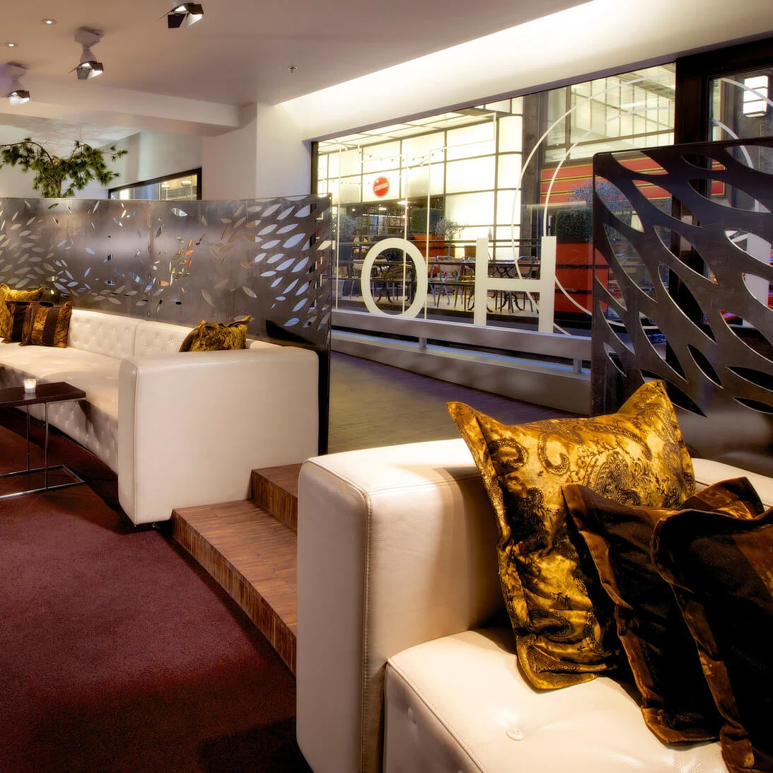 En moderne lounge med skinnsitteplasser, dekorative metallskjermer, stemningsbelysning, og luksuriøse puter i et elegant interiør.