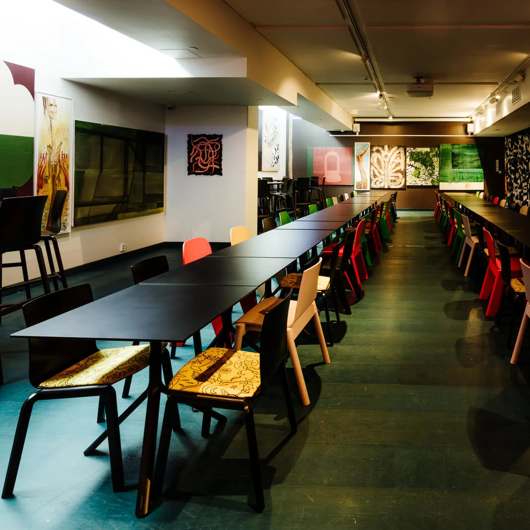 Long black tables lined with colorful chairs, set in a room with patterned curtains and modern art on the walls, creating a vibrant and eclectic meeting space.