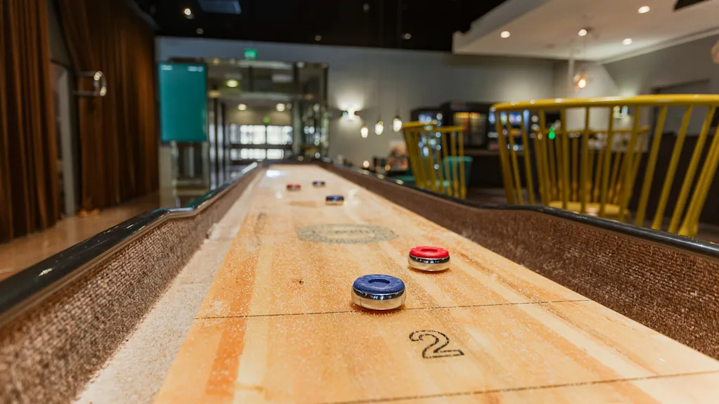 A shuffleboard game with red and blue pucks and the number 2 on the table, set in a modern and inviting lounge.