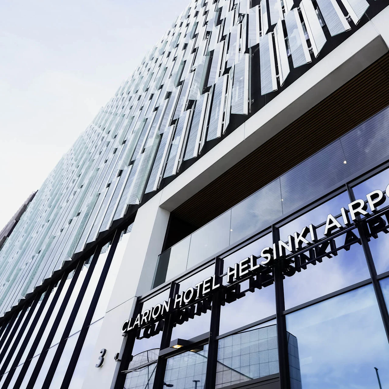 Clarion Hotel Helsinki Airport facade with glass windows reflecting the sky, featuring modern architectural design. 