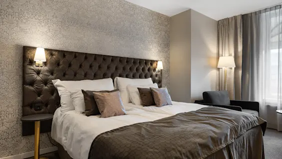 Et hyggeligt og elegant indrettet hotelværelse med en stor seng, blød belysning og komfortable siddepladser.