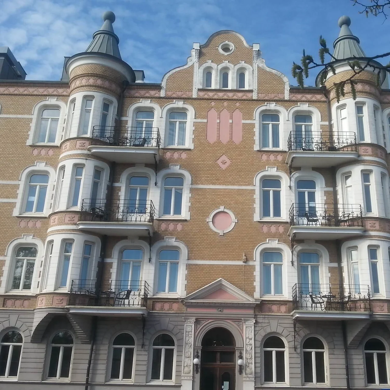 A multi-story ornate building with balconies, domed towers, and a clear sky backdrop.