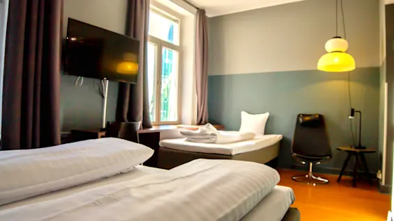 Ett bekvämt hotellrum med två sängar, ett stort fönster, en TV och en modern gul lampa.