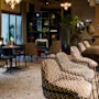 Elegant bar stools are positioned along a sleek counter in a stylish dining area; the background features tables, chairs, and decorative lighting, creating a sophisticated ambiance.