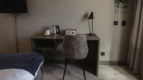 Ett hotellrum med skrivbord, stol, vattenkokare, radio och lampa, plus en väggmonterad TV, för en bekväm vistelse.