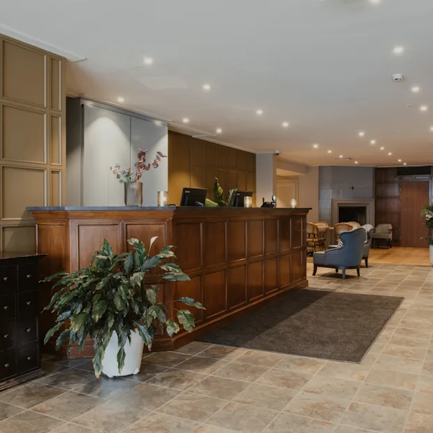 En varm og indbydende hotellobby med en reception i træ, komfortable siddepladser og en hyggelig pejs.