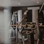 Moderni kuntosali, jossa etualalla kuntopyörä ja taustalla muita treenilaitteita. Näytöllä lukee PAUSE START.