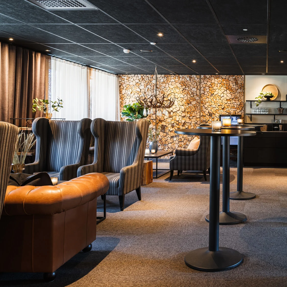 Modern lounge med eleganta stolar runt bord; shuffleboardbord i förgrunden. Väggar med trädetaljer, med stämningsbelysning och dekorativa växter som förhöjer den mysiga atmosfären.
