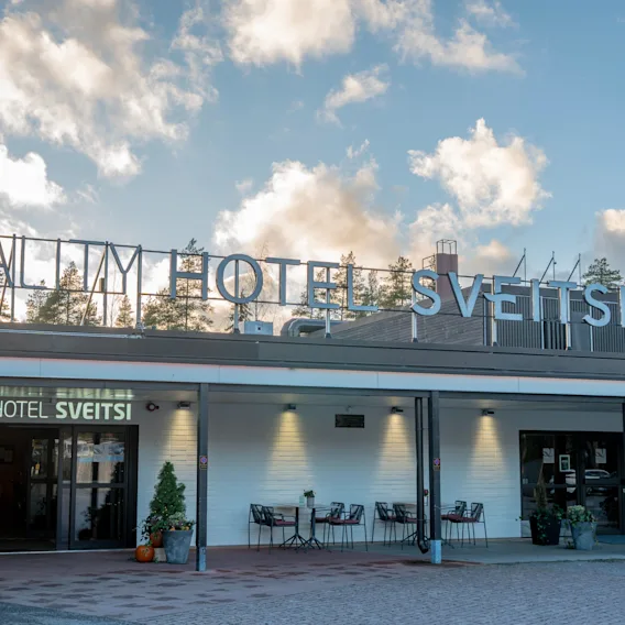 Kutsuva näkymä Quality Hotel Sveitsin ulkoasusta, jossa on ulkoistuimia ja kausikoristeita pilvisen taivaan alla.