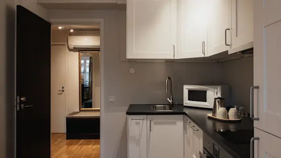 A compact kitchen area with white cabinets and a black countertop, leading to an entryway. Home Hotel Kung Oscar.