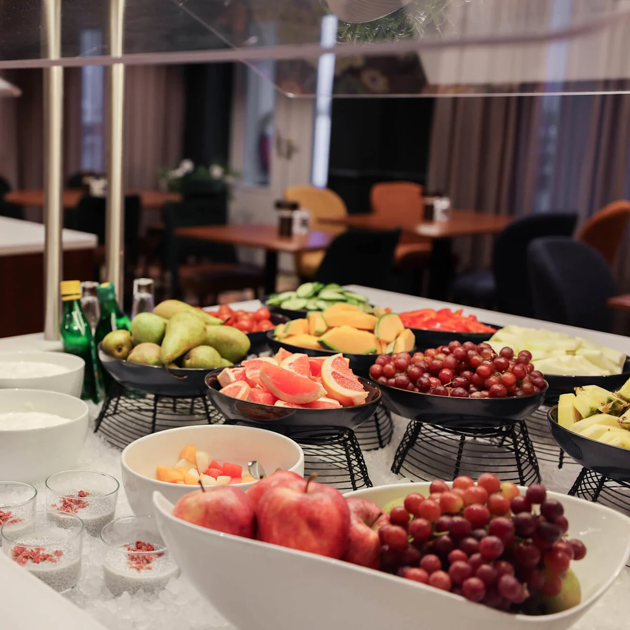 Fruit and yogurt buffet; bowls of assorted fruits and yogurt are arranged on ice in a dining area with tables and chairs in the background.