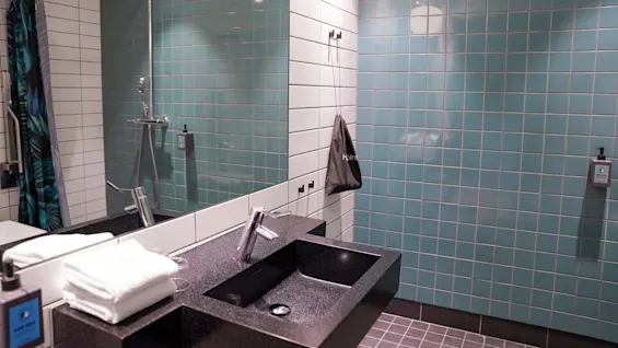 Et moderne bad med en sort benkeplatevask, speil, og dusjområde omsluttet av glassvegger med blågrønne fliser.