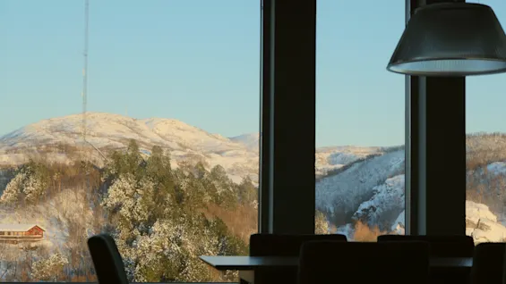 Et fredfyldt vinterlandskab med snedækkede bjerge og træer, set fra et vindue med silhuetter af indendørsmøbler.