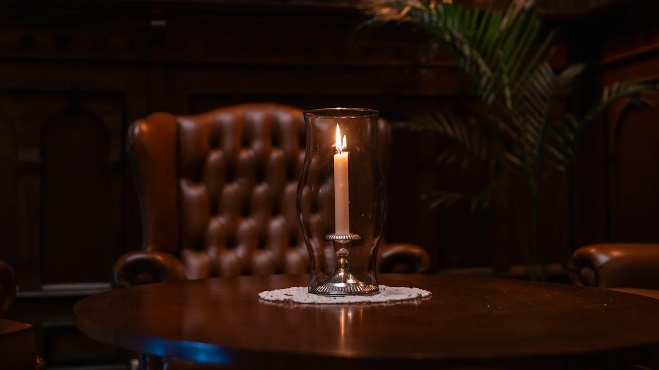 A cozy corner in Dalen Hotel featuring a candle in a glass holder on a wooden table, casting a warm glow against a leather armchair and rich wooden paneling.