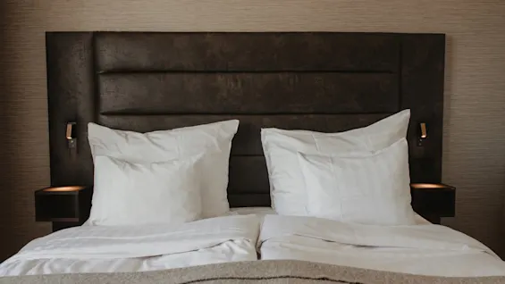 Mukava hotellisänky valkoisilla liinavaatteilla ja tummalla sängynpäädyllä Home Hotel Victoriassa, valmiina lepoon.